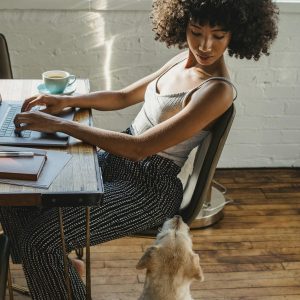 African American woman working on computer with dog near
