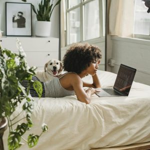Relaxed black woman watching laptop near dog on bed